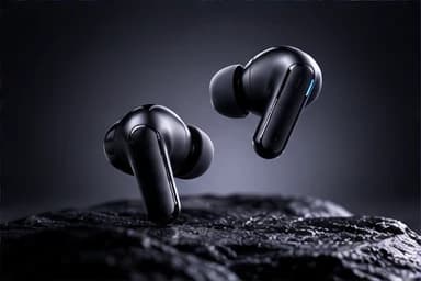 A pair of black wireless earbuds above a dark stone surface under a soft spotlight