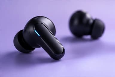 Close-up of a black wireless earbud on a lavender background, its status light glowing